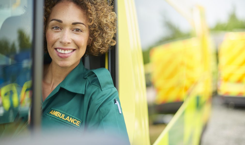 uk ambulance staff members in her ambulance. She is wearing green ambulance uniform typical of uk paramedics. She is sitting in the ambulance ready to go to a call